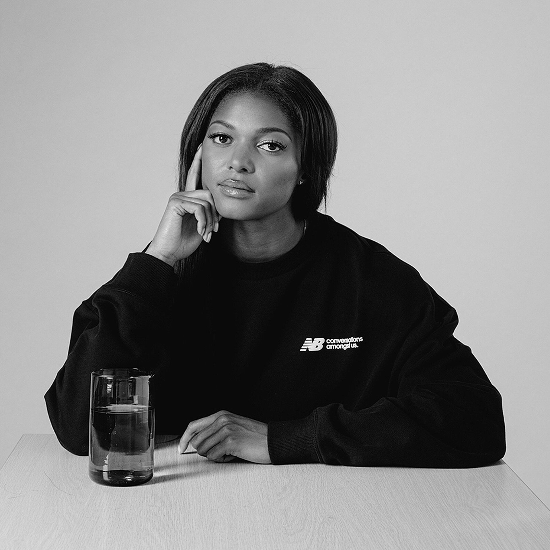 Black and white portrait of Gabby Thomas posed at table with glass of water